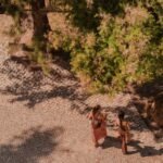 Aerial shot of two people walking on a cobblestone path in a sunny Lisbon park under trees.